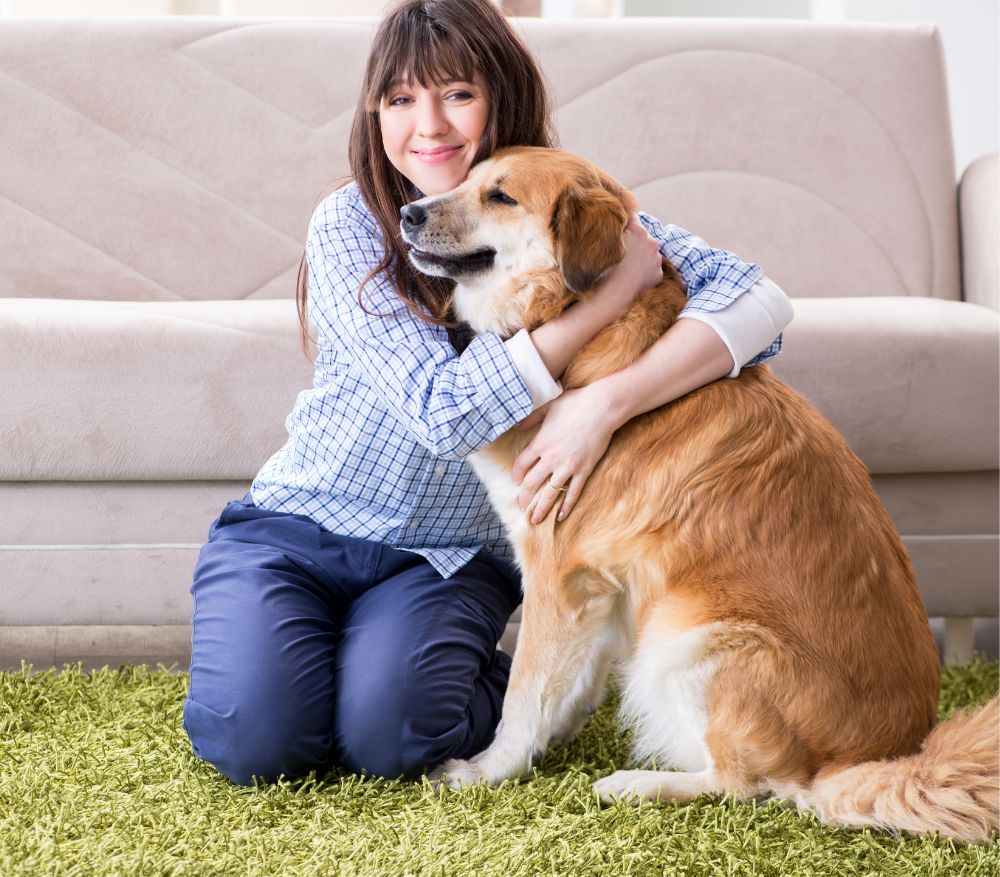 A smiling person in a blue plaid shirt pets a golden retriever in a bright, modern kitchen